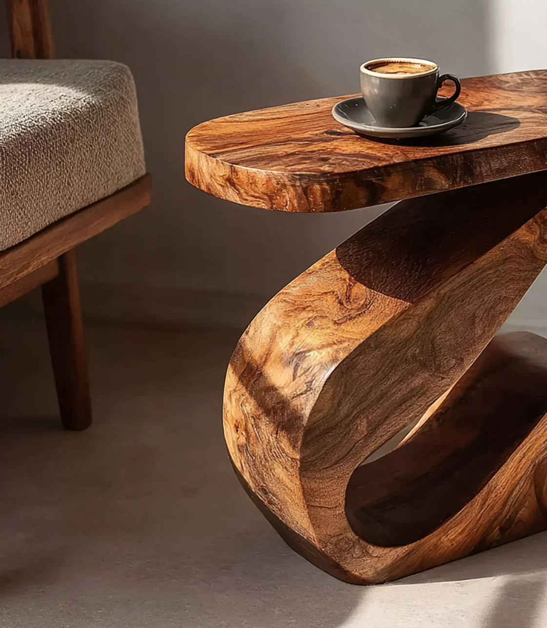 Curved wooden coffee table with natural grain holding a cup of coffee, beside a textured fabric chair