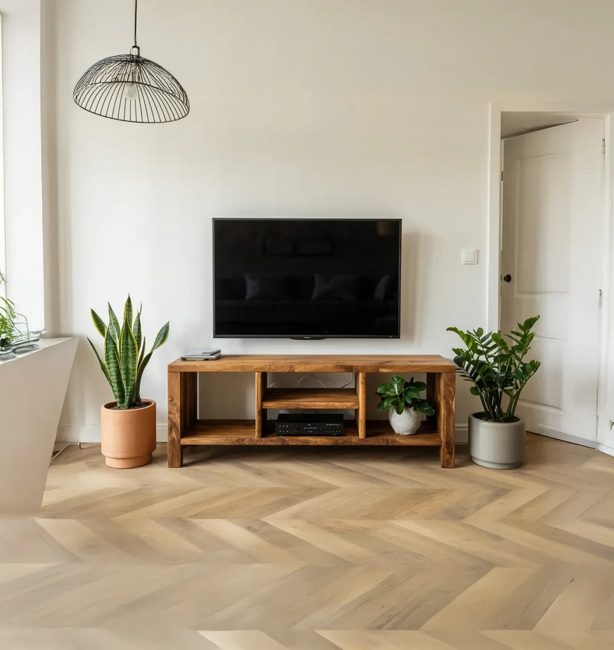 Minimalist living room with wall-mounted TV, wooden media console, two potted plants, and modern light fixture