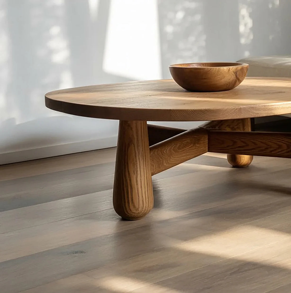 Solid wood coffee table with rounded legs and matching wooden bowl in sunlit living room