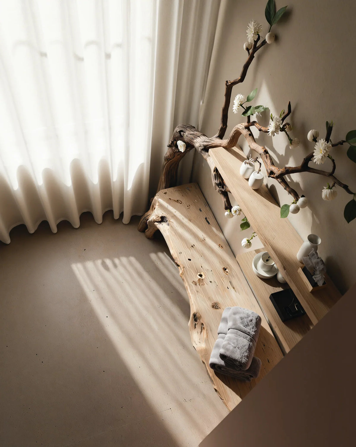 Live edge wooden bench and floating shelf with decorative branch and flowers in sunlit room