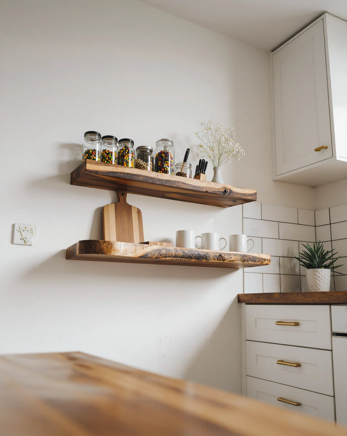 Solid wood live edge floating shelves in modern kitchen holding jars, mugs, and decor