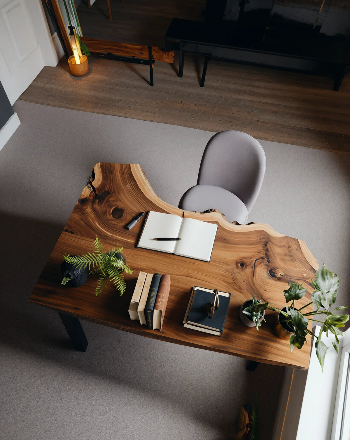 Live edge solid wood desk with plants, books, and open notebook in a modern home office