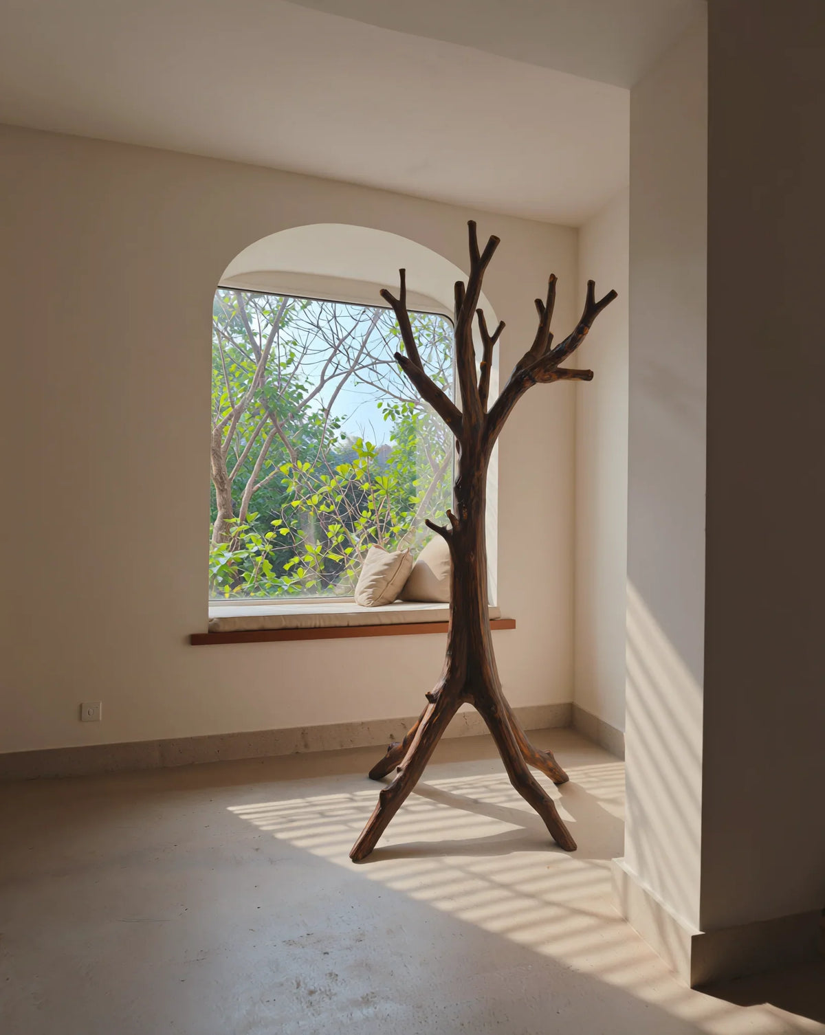 Solid wood tree coat rack in sunlit minimalist room with window seat and greenery outside