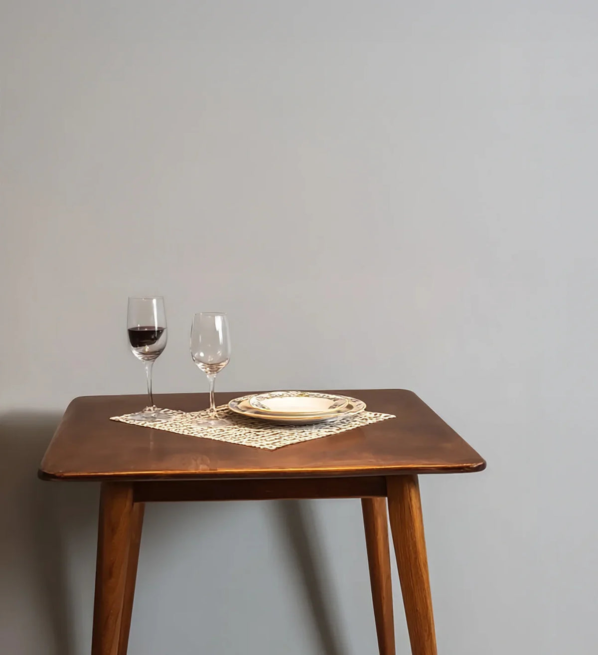 Solid wood dining table with two wine glasses and ceramic plates on placemats