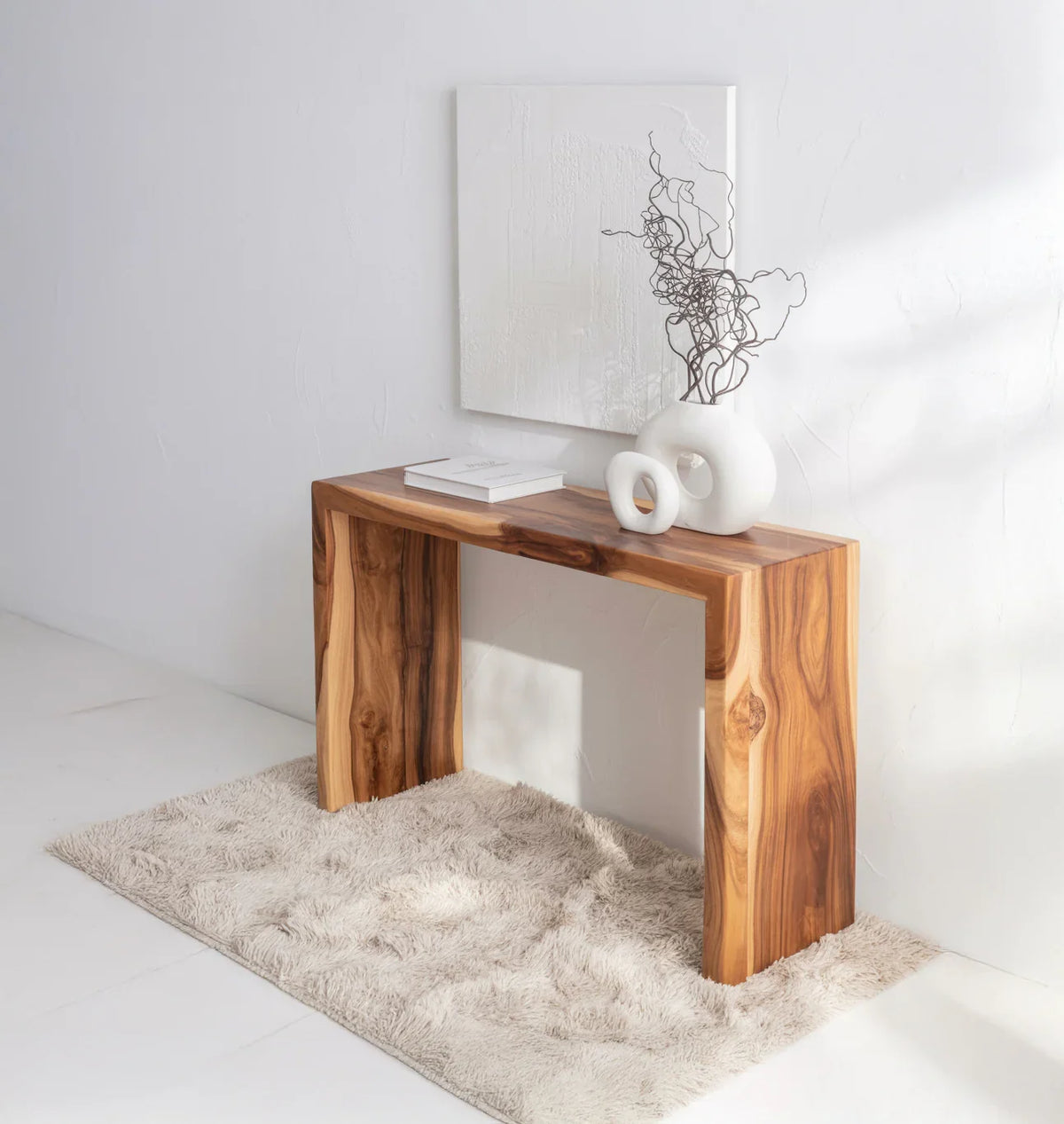Minimalist solid wood console table on a plush rug, styled with modern ceramic vases and books.