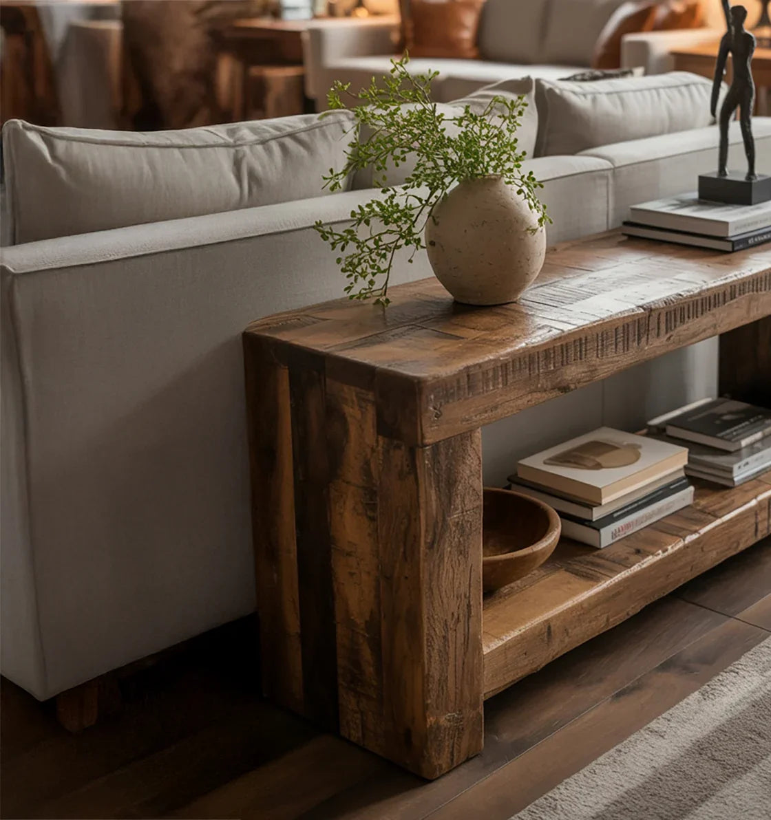 Rustic wooden console table behind beige sofa with potted greenery and stacked books in cozy living room