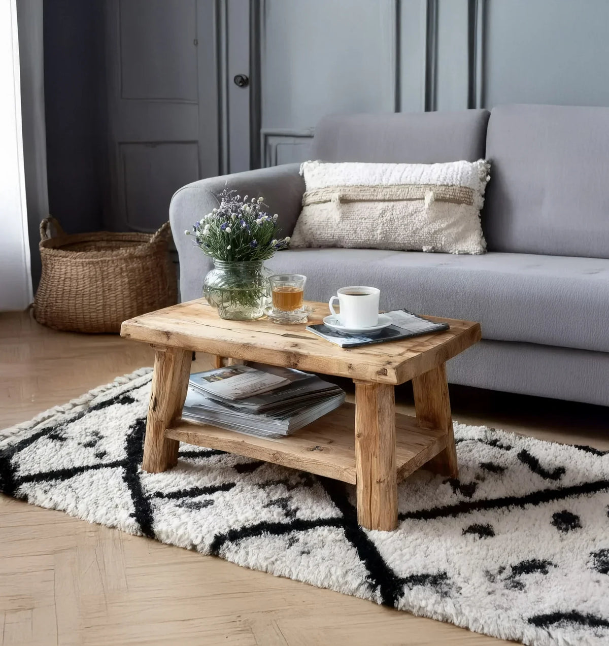 Cozy living room with gray sofa, wooden coffee table, textured pillow, vase with flowers, and patterned rug