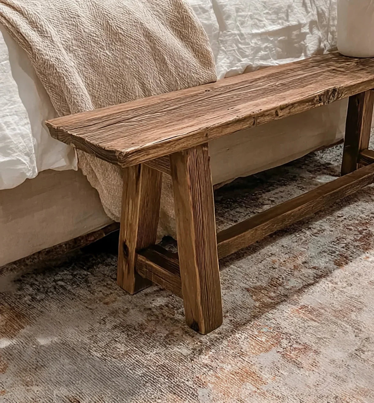 Rustic wooden bench with visible grain texture on patterned rug next to beige sofa with blanket