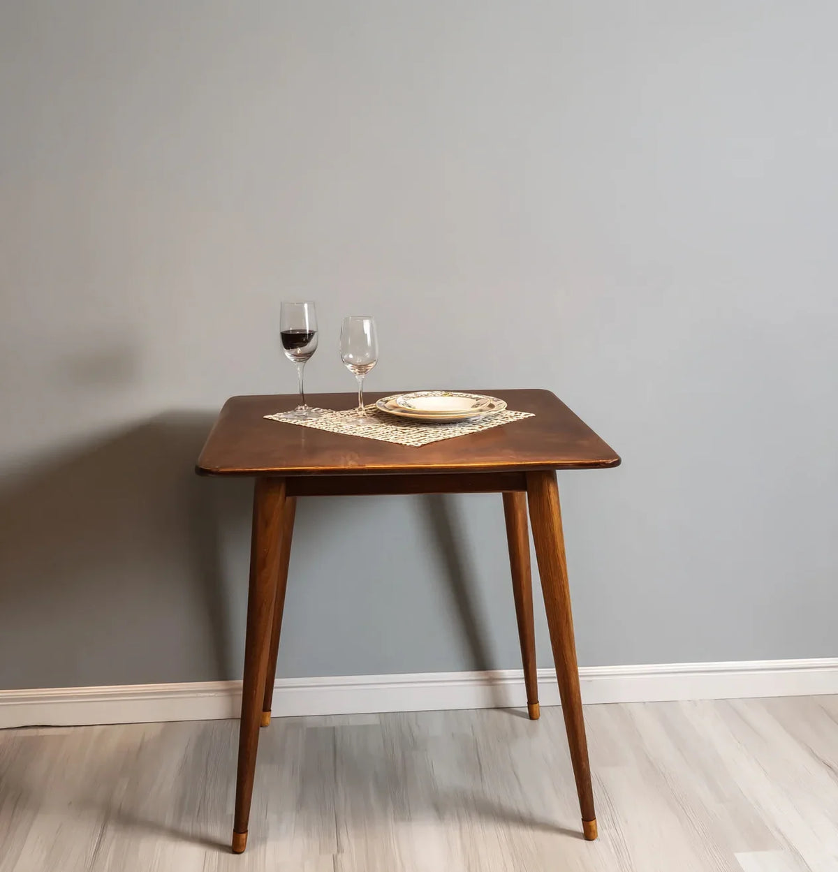 Solid wood dining table with tapered legs, set with wine glasses and plate on a mat