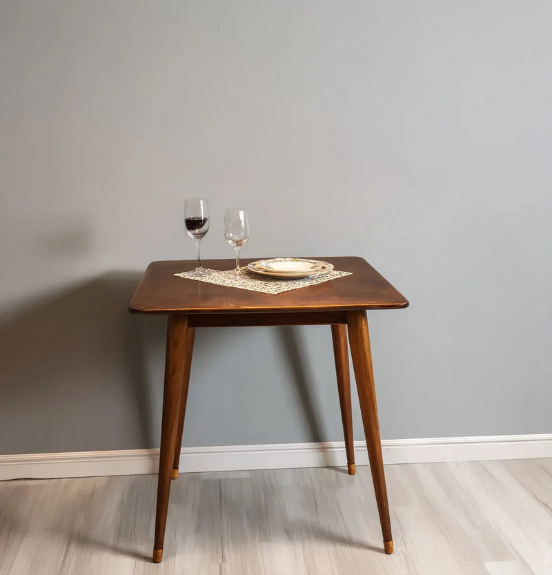 Solid wood dining table with tapered legs, set with wine glasses and plate on a mat