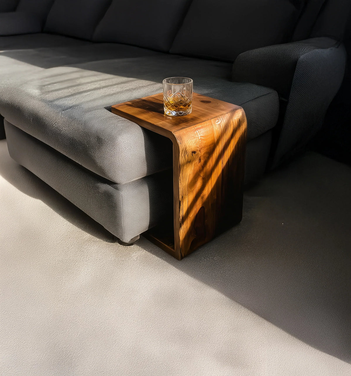 Grey fabric sofa with a curved wooden side table holding a glass of whiskey, sunlight and shadows