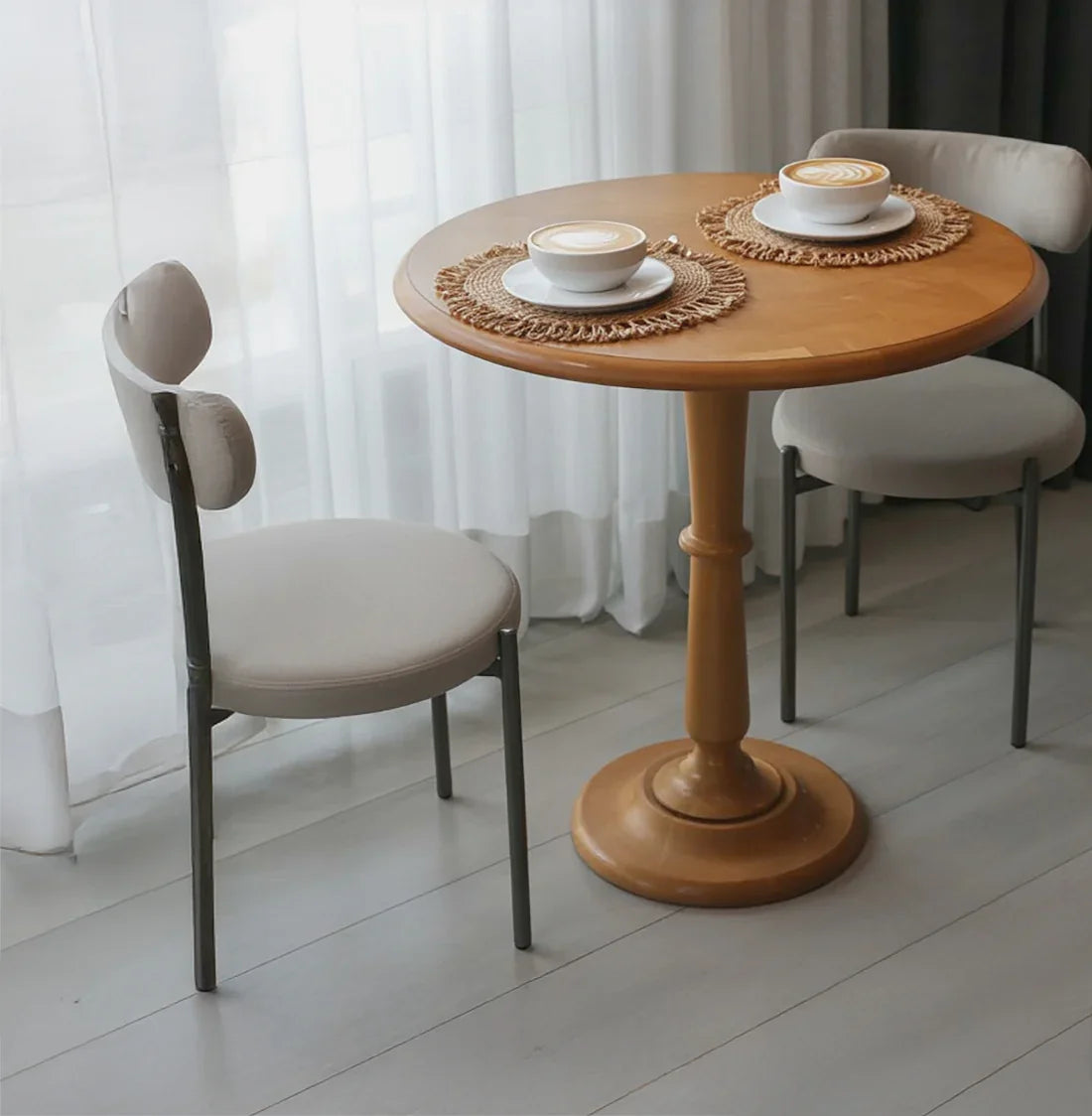 Round solid wood table with two cushioned chairs and lattes in a bright room