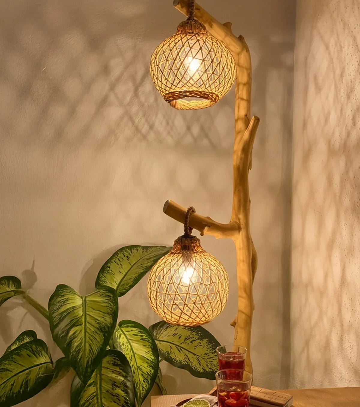 Handcrafted wooden floor lamp with woven rattan shades, surrounded by green plant leaves