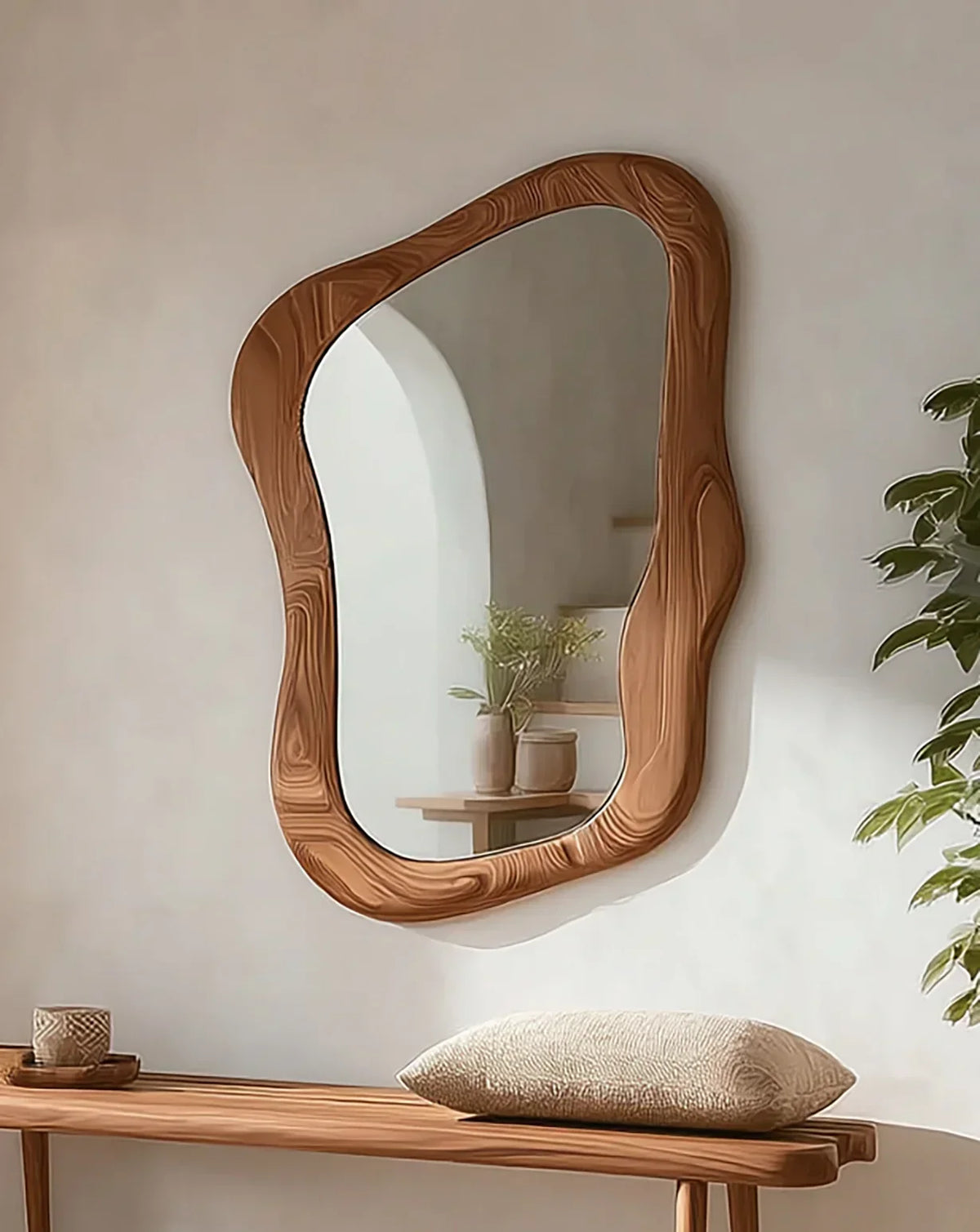 Organic shaped wood frame mirror above wooden bench with cushion and decor in modern room