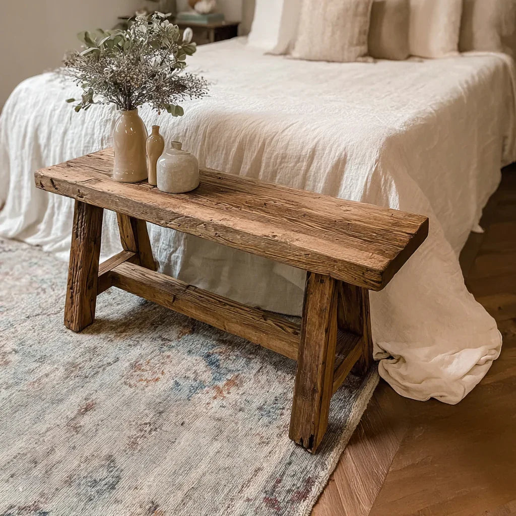 Rustic wooden bench with ceramic vases and dried flowers at bed foot in cozy bedroom