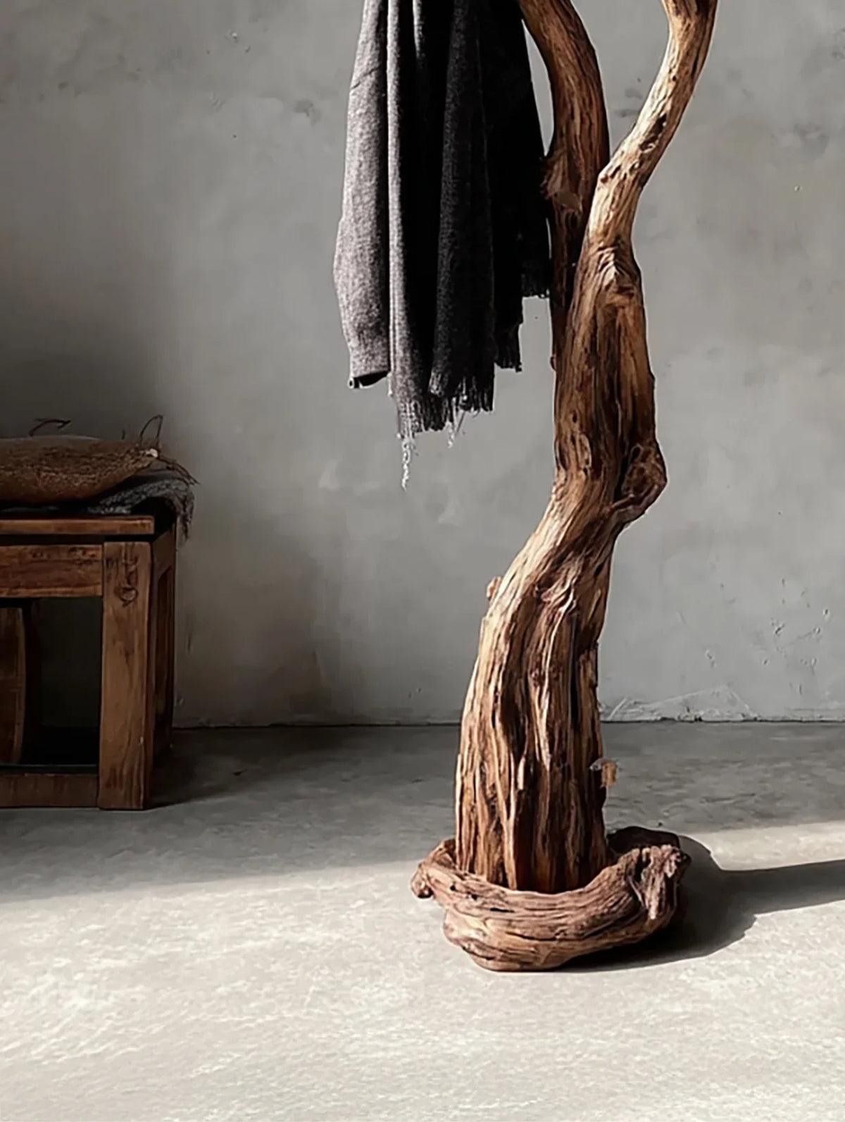 Rustic wood coat rack with dark gray scarf in minimalist room with wooden bench and concrete floor