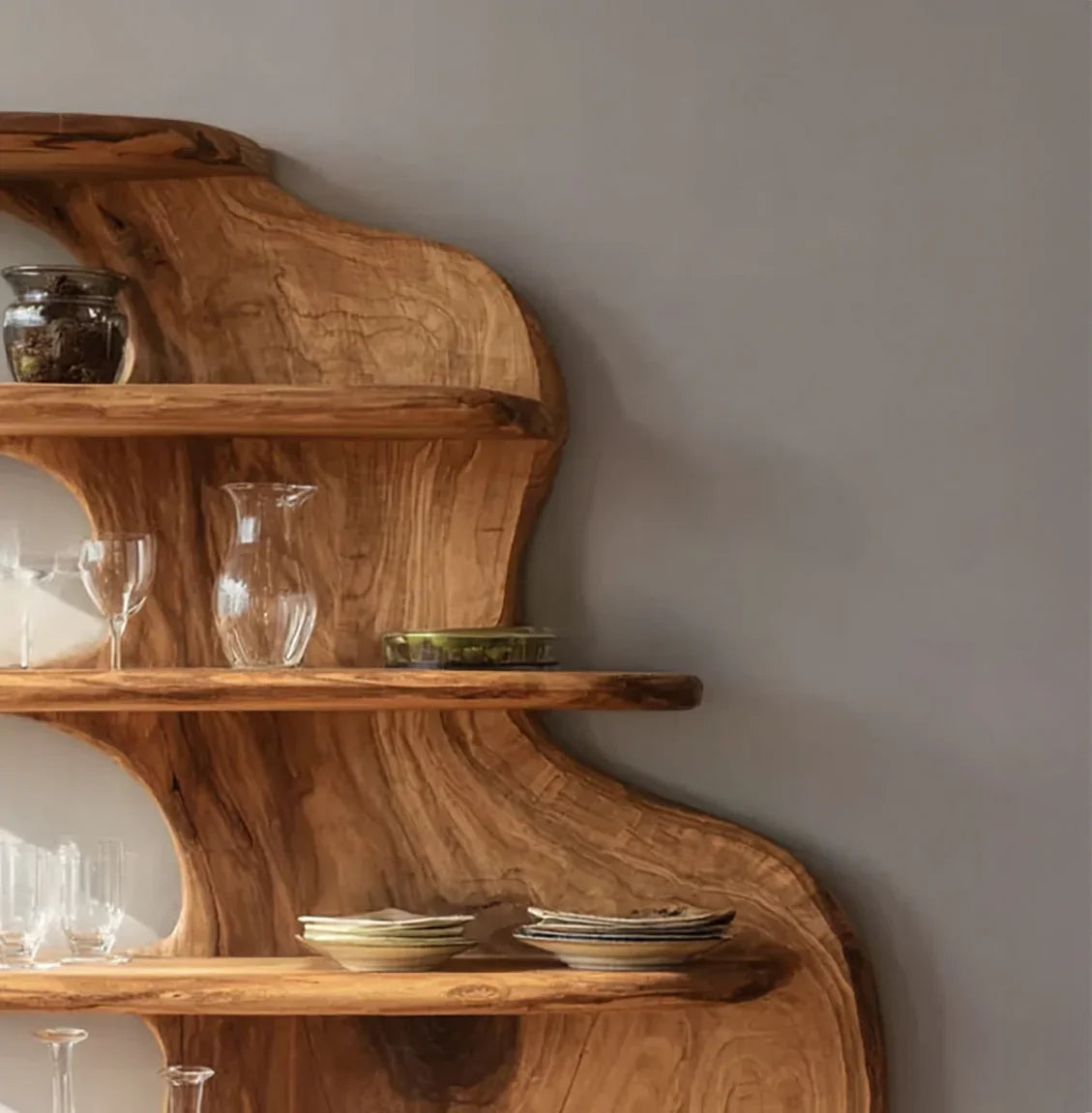 Rustic wooden wall shelf with glassware and ceramic plates against gray wall