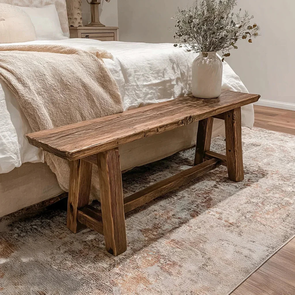 Rustic wooden bench at bedroom foot with white vase and dried flowers on patterned rug
