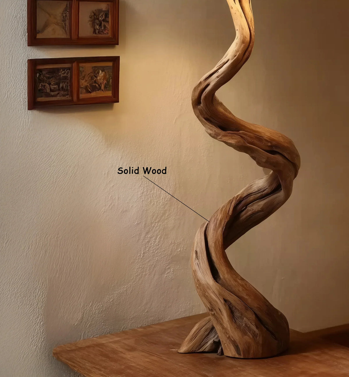 Twisted solid wood sculpture on wooden table with framed pictures on textured wall