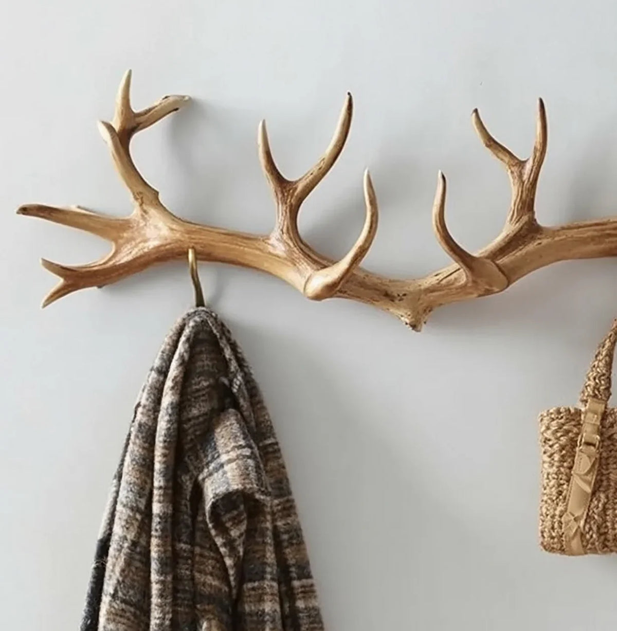 Wall-mounted rustic antler coat rack with hooks, holding a striped jacket and woven bag