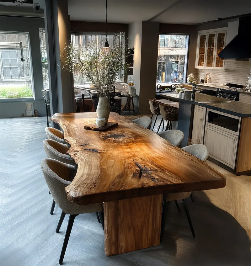 Modern dining room with large live edge wooden table, upholstered chairs, and decorative vase with branches