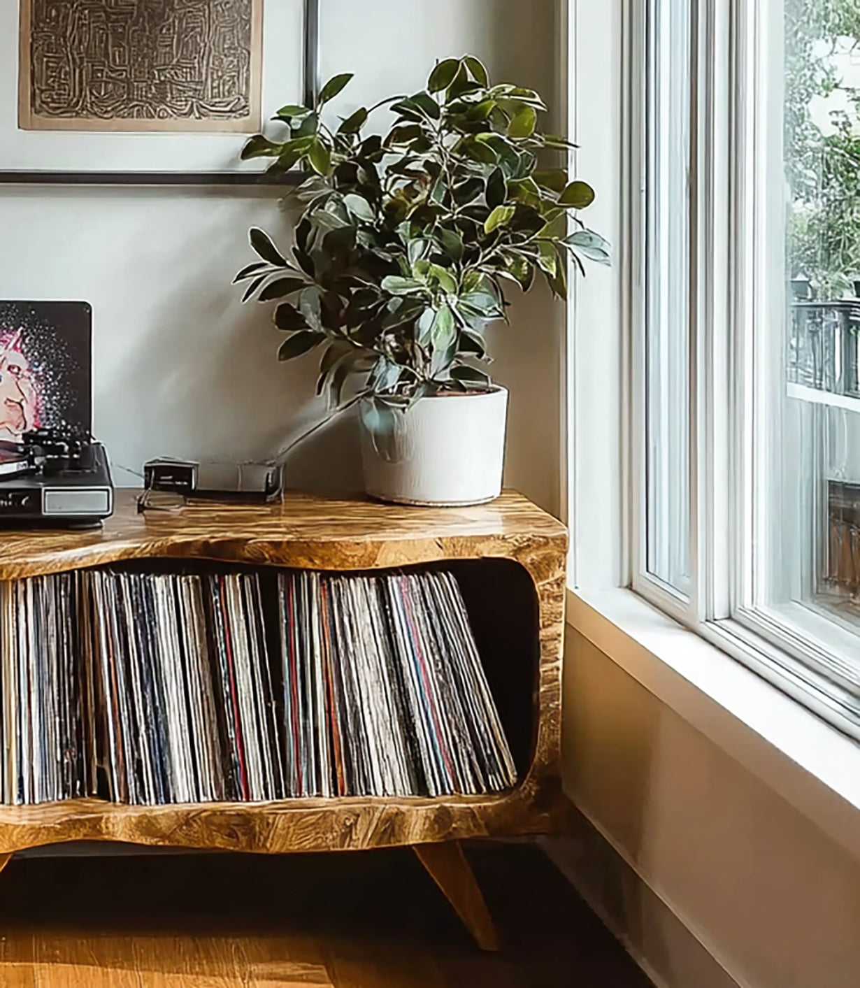 Wooden mid-century cabinet with vinyl records, turntable, and green potted plant by bright window