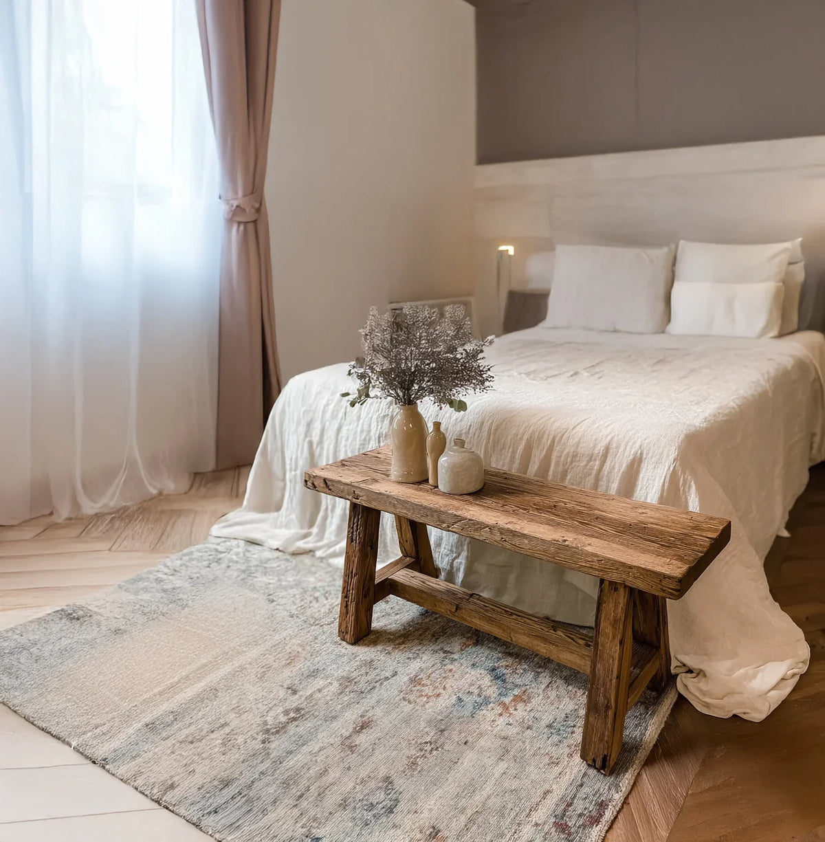Cozy bedroom with rustic wooden bench, neutral bedding, ceramic vases, and soft natural lighting