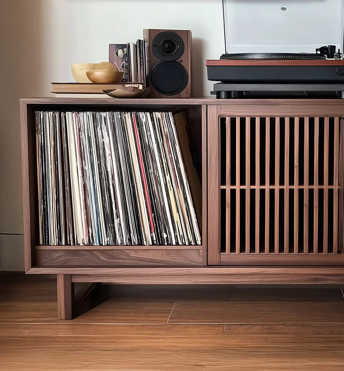 Wooden record player cabinet with vinyl records, speaker, and decorative bowls on top