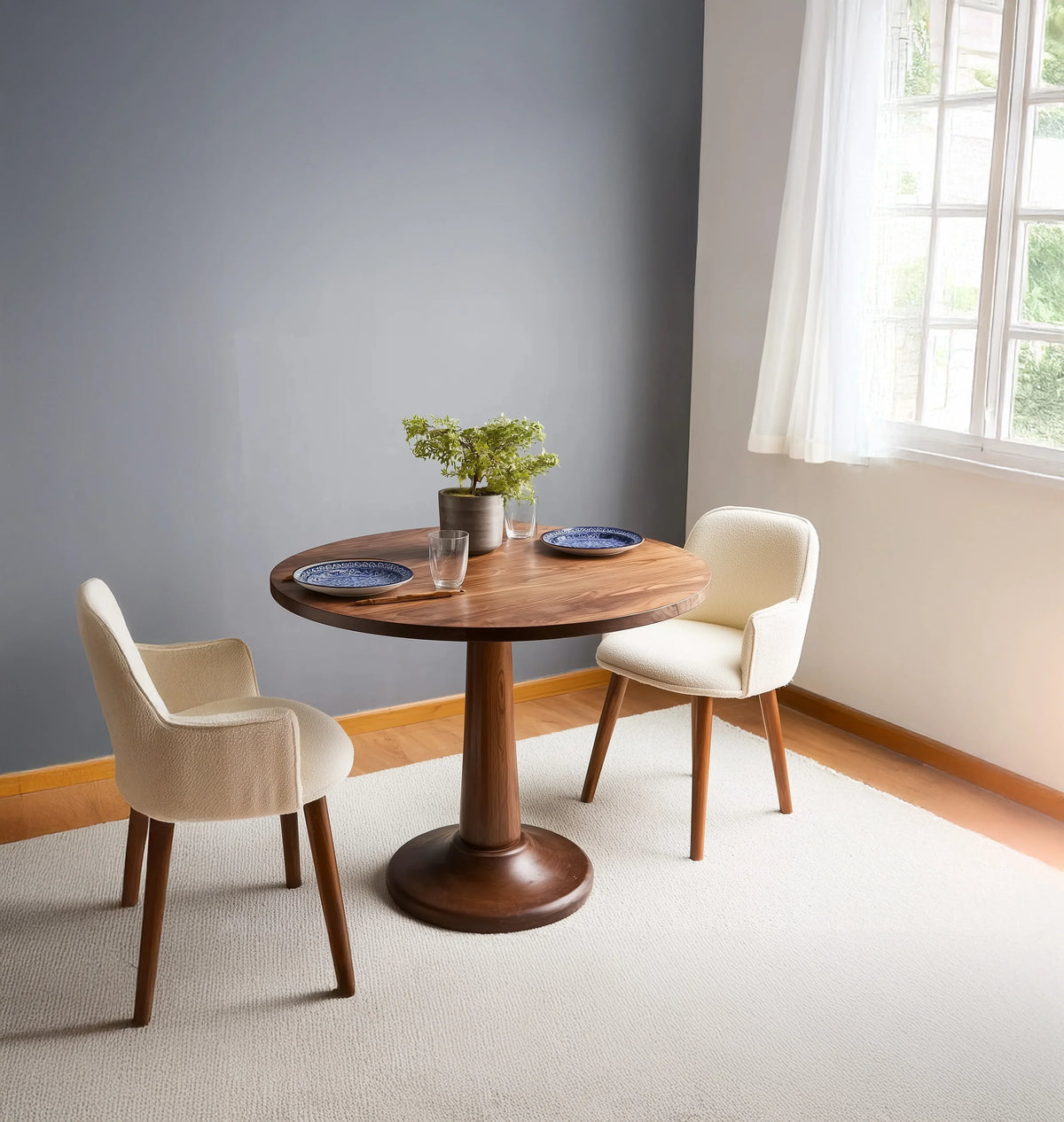 Round solid wood dining table with pedestal base and two modern cream chairs in bright room