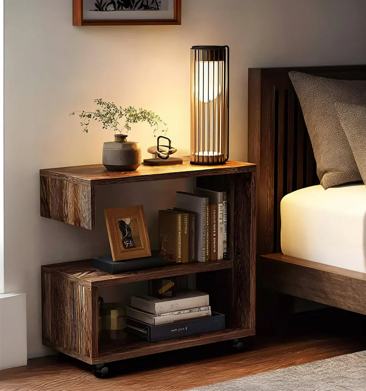 Solid wood nightstand with open shelves, books, modern lamp, and decor beside bed