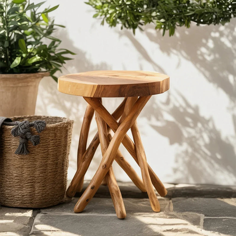 Round wooden side table with natural twisted legs on stone tile floor, next to woven basket and potted plant