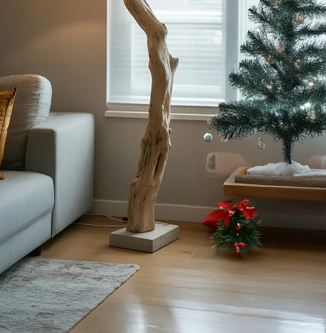 Cozy living room corner with gray sofa, natural wood floor lamp, small decorated Christmas tree, and festive decor
