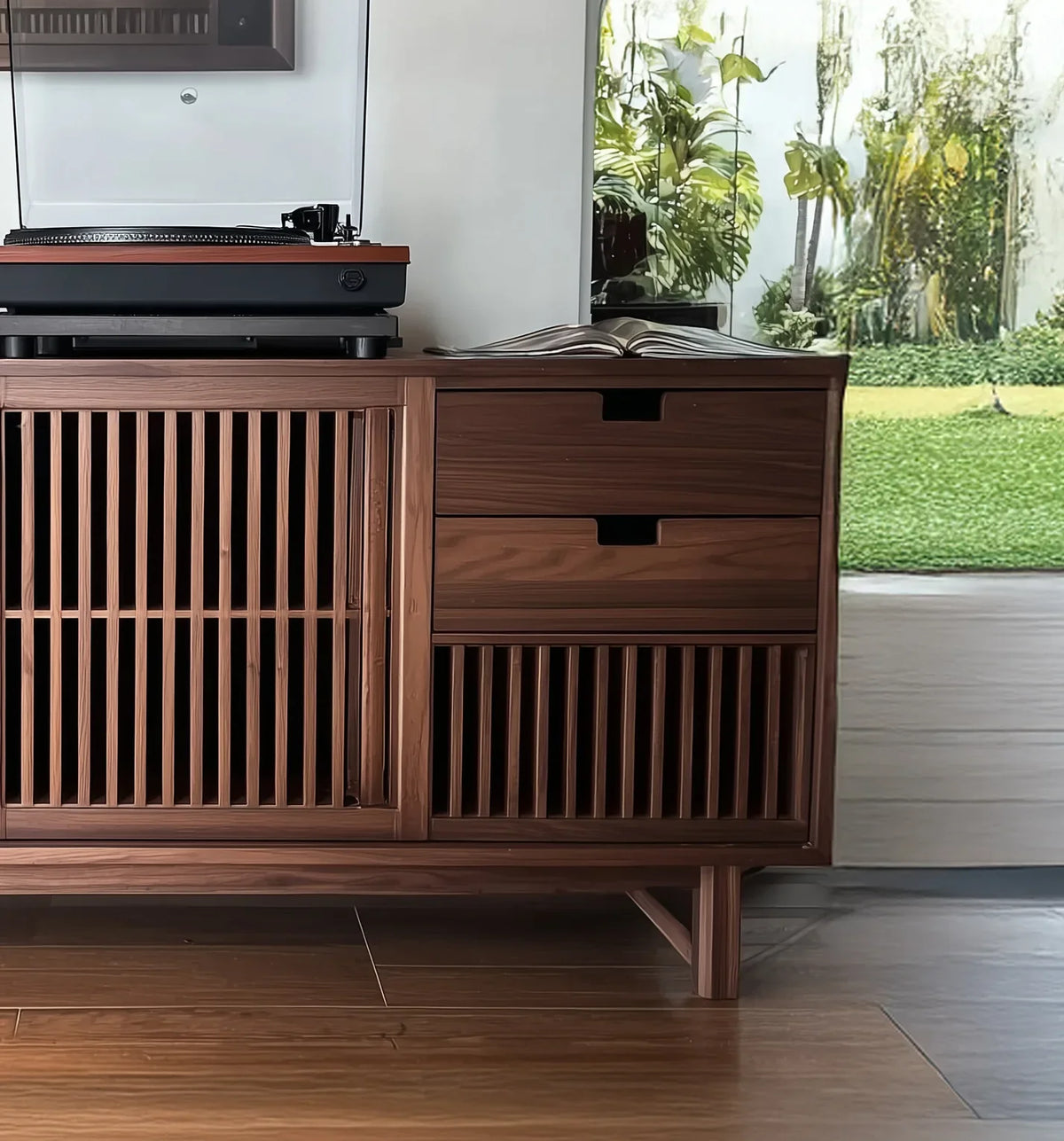 Modern wooden cabinet with slatted doors, two drawers, turntable on top, and a book in bright room