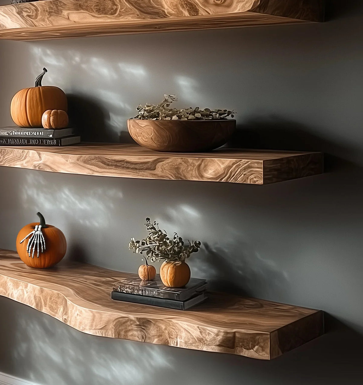 Floating wooden shelves decorated with pumpkins, skeleton hand prop, dried plants, and books on gray wall