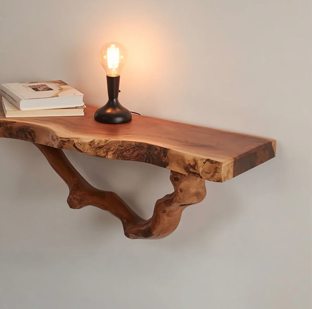 Live edge floating wood shelf with a branch support, table lamp, and books on wall
