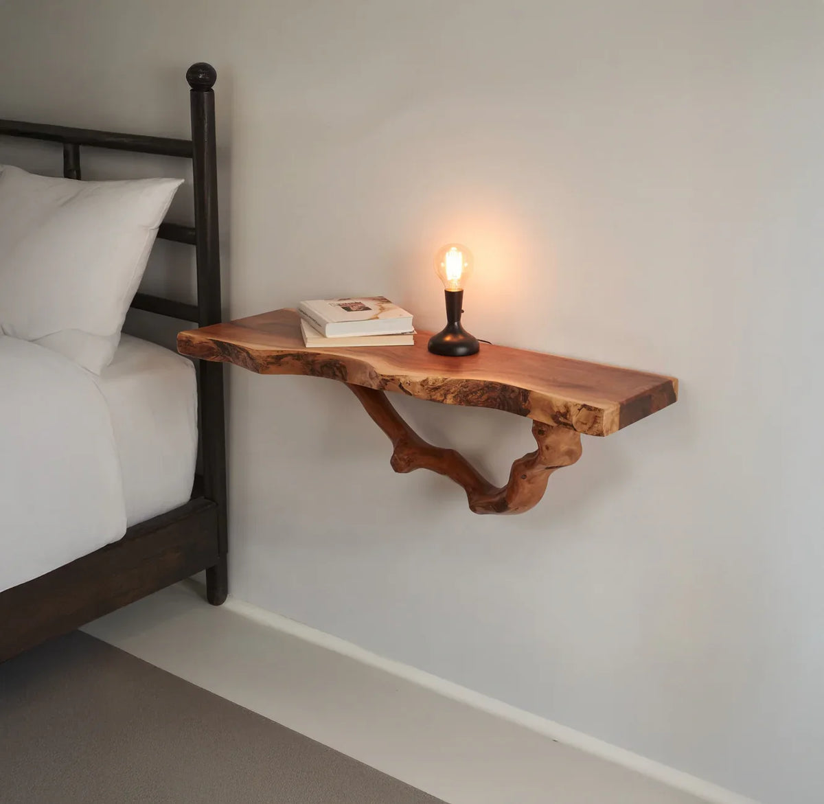 Live edge solid wood floating nightstand with lamp and books beside a bed