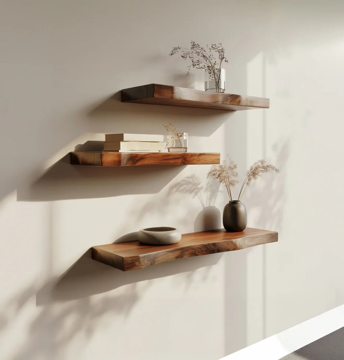 Three solid wood floating shelves with live edge design, decorated with books, vases, and dried plants.