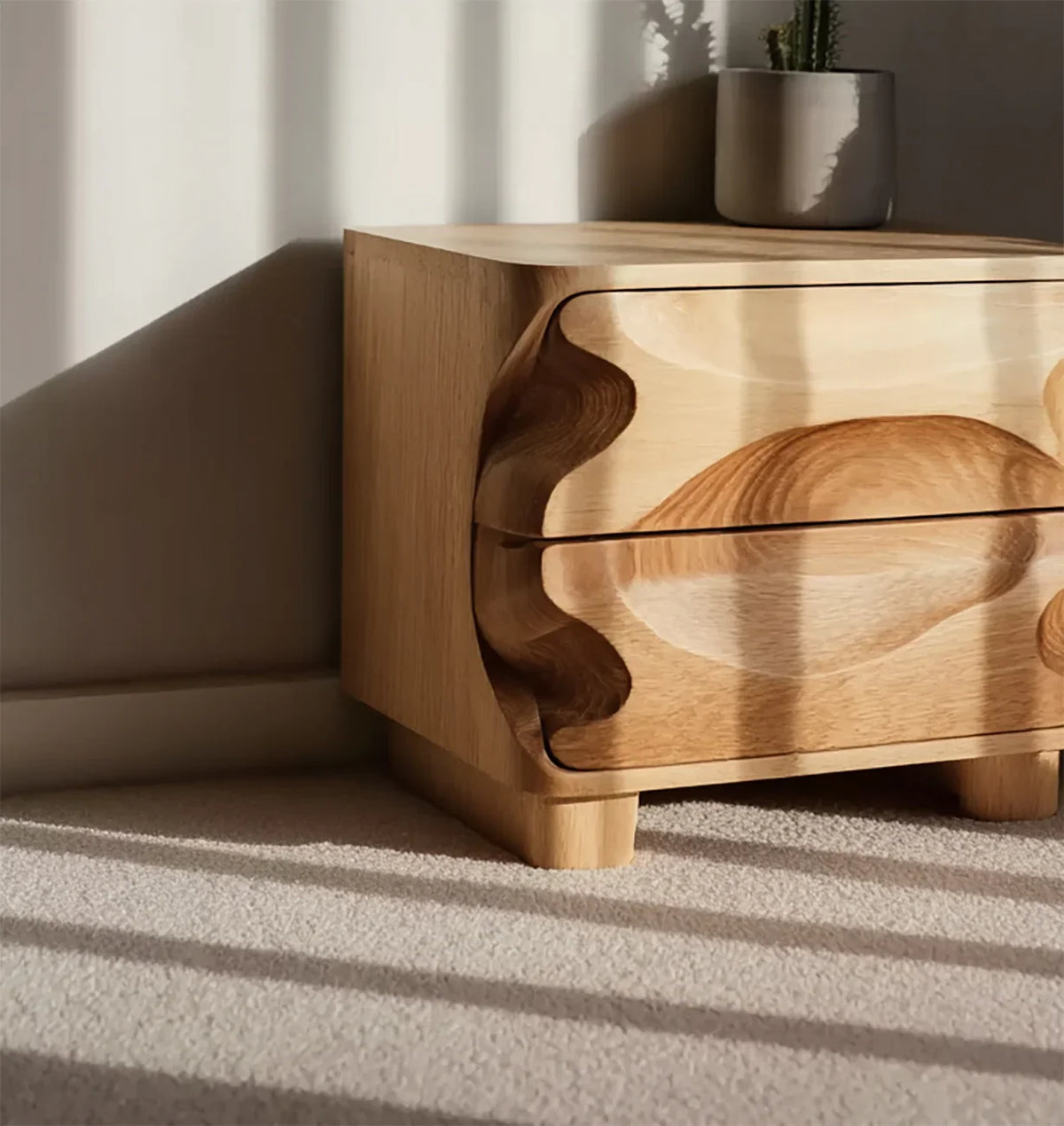 Modern wooden nightstand with carved drawers in sunlight on carpeted floor, plant on top
