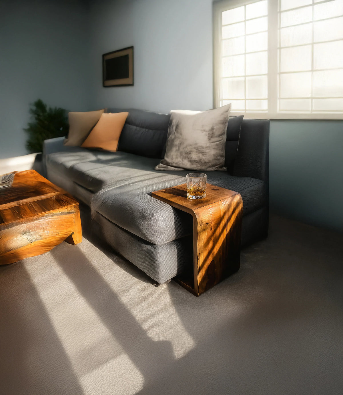 Modern gray sofa with pillows beside natural wood coffee and side tables in sunny living room