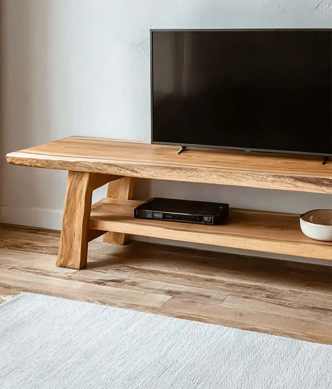 Modern wooden TV stand with flat screen TV, media player, and decorative bowl on rustic wooden floor