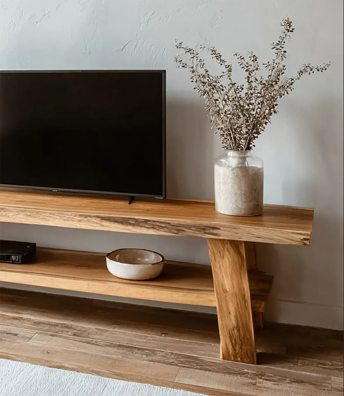 Modern wooden TV stand with flat screen TV, beige ceramic bowl, and glass vase with dried branches