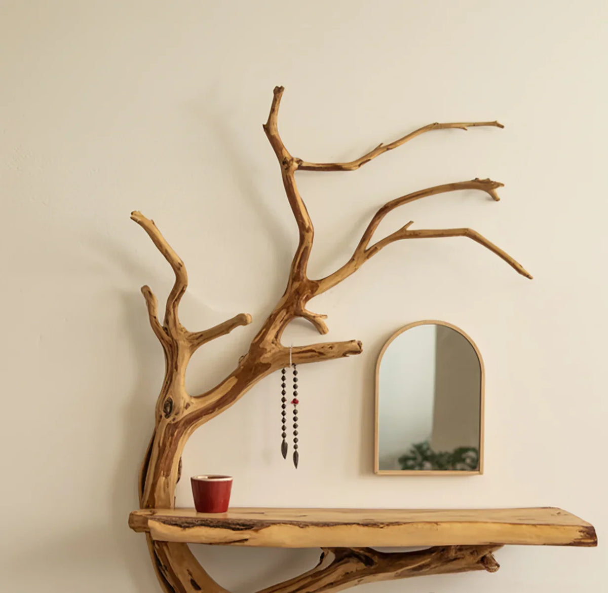 Live edge wood tree bookshelf with branch design, red cup, and arched mirror on wall.