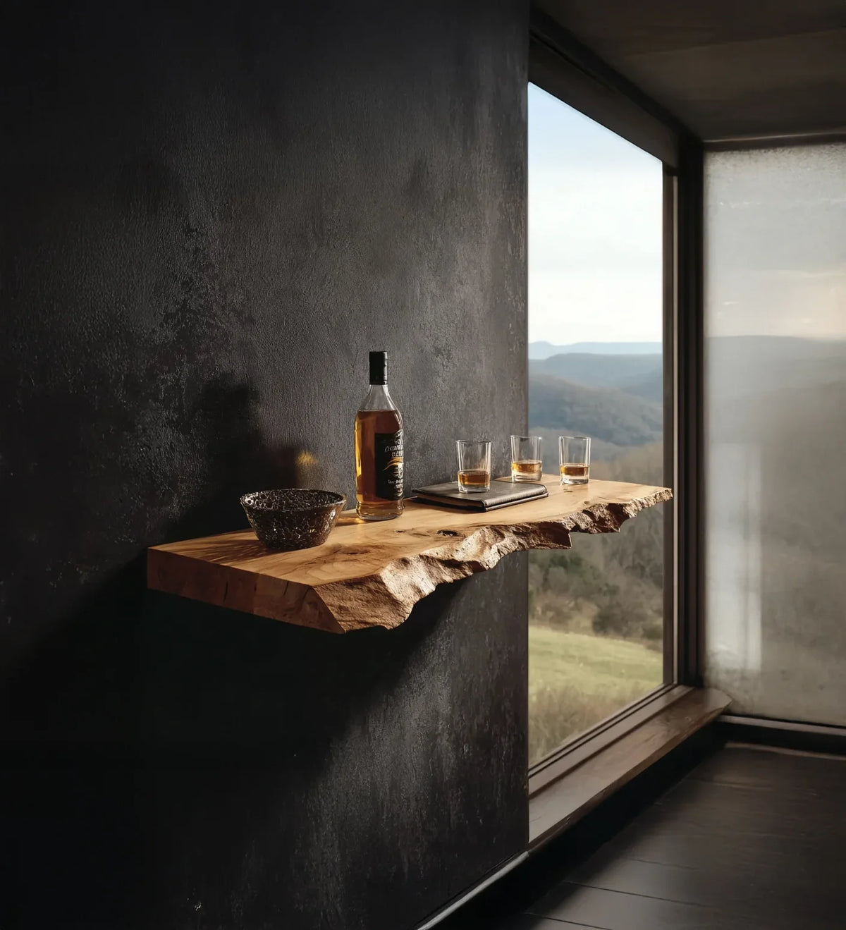 Rustic wooden shelf with whiskey bottle, three glasses, and bowl against dark wall near window with mountain view