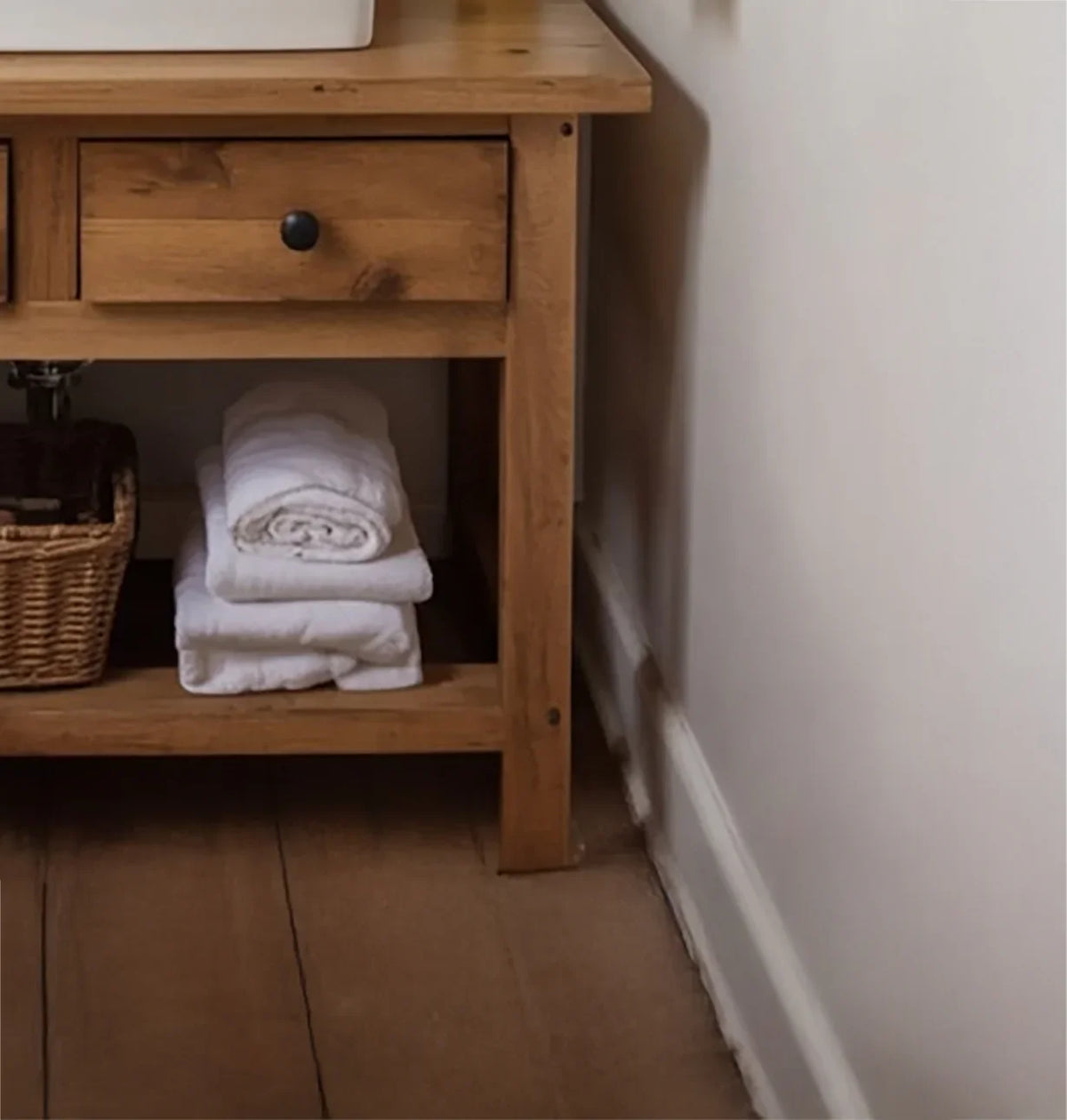 Solid wood bathroom vanity with drawers, stacked white towels, and woven storage basket