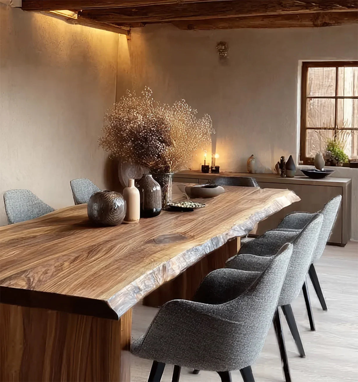Modern rustic dining room with large live edge wooden table, gray upholstered chairs, and dried floral centerpiece