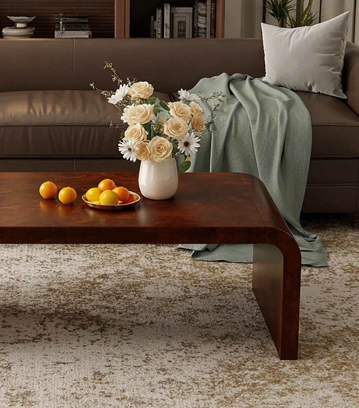 Brown leather sofa with gray pillow and green throw blanket, wooden coffee table with flowers and oranges