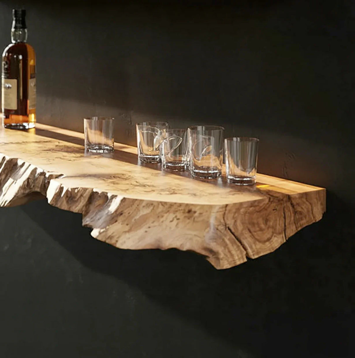 Live edge floating wood shelf mounted on wall, holding whiskey bottle and glass tumblers