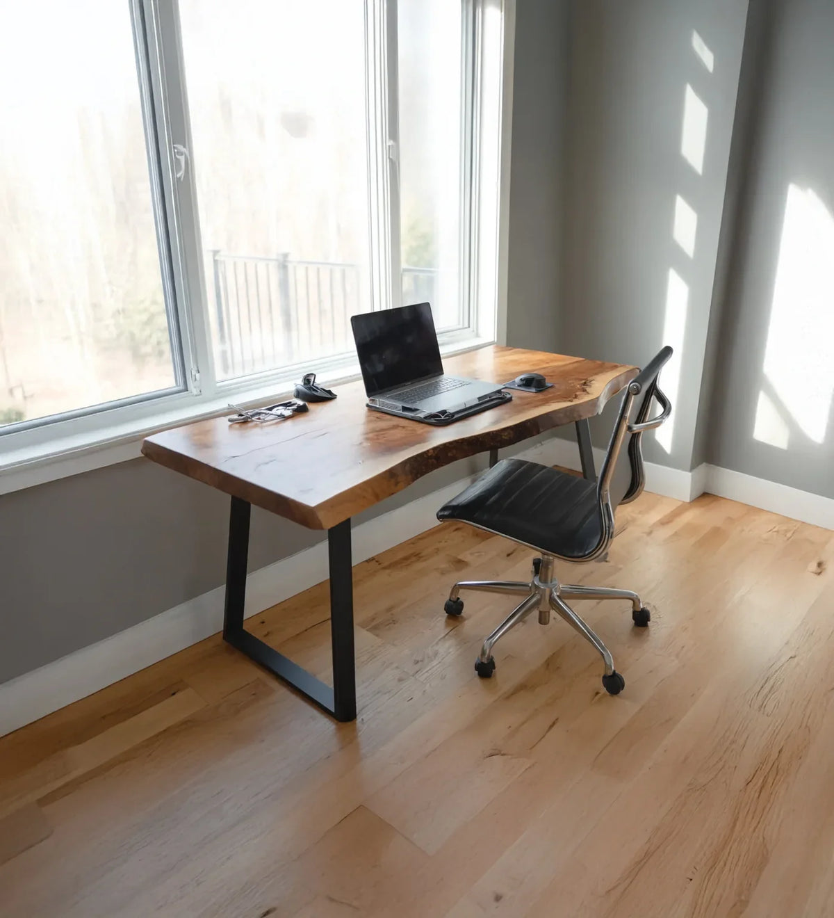 Modern home office with live edge wooden desk, laptop, black ergonomic chair, and large window