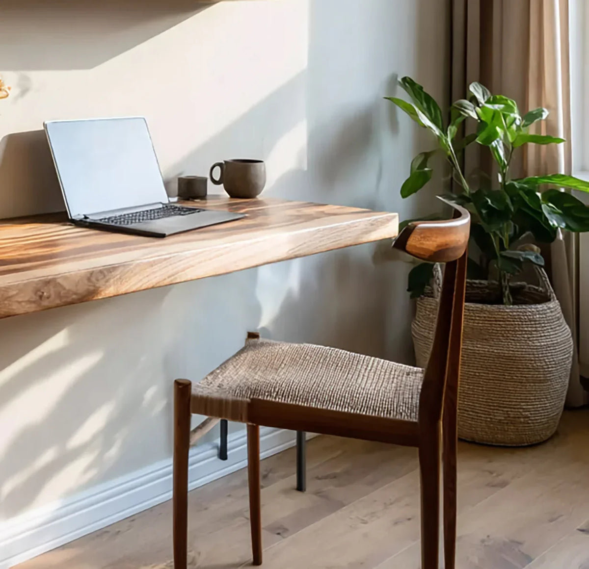Live edge wood floating desk with laptop, ceramic cup, woven chair, and potted plant in sunlight