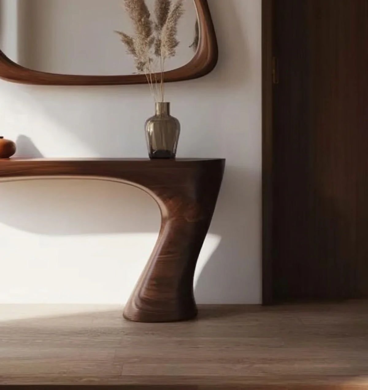 Modern wooden console table with organic curves, glass vase with pampas grass, and oval wall mirror